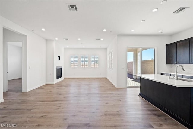 kitchen with light countertops, a glass covered fireplace, a sink, and visible vents