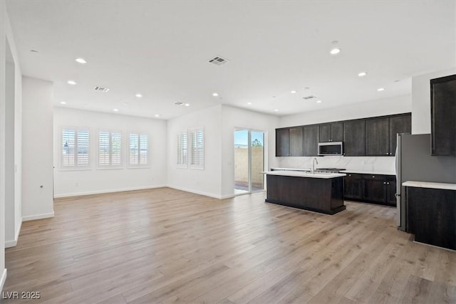 kitchen featuring light wood finished floors, light countertops, stainless steel microwave, visible vents, and open floor plan