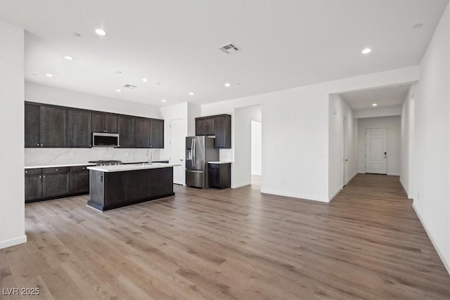 kitchen featuring dark brown cabinetry, stainless steel appliances, visible vents, light wood-style floors, and open floor plan