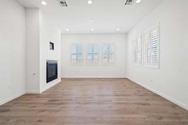 unfurnished living room with light wood-style floors, a glass covered fireplace, visible vents, and recessed lighting