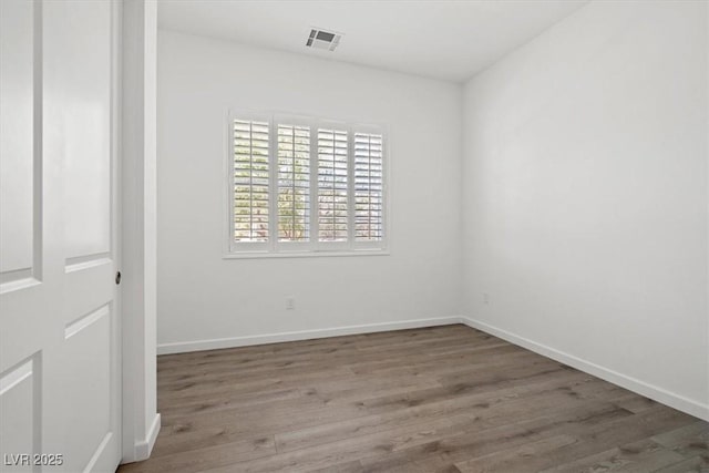 empty room featuring wood finished floors, visible vents, and baseboards