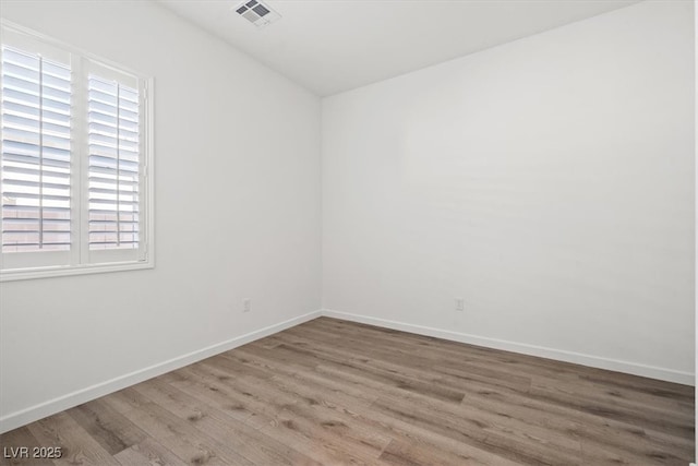 empty room featuring wood finished floors, visible vents, and baseboards