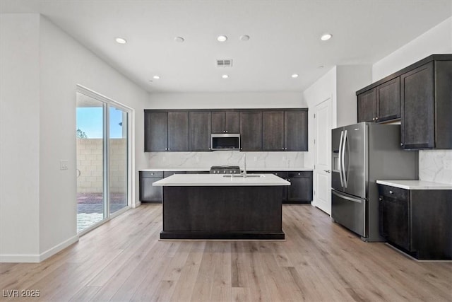 kitchen with light wood finished floors, stainless steel appliances, tasteful backsplash, light countertops, and visible vents