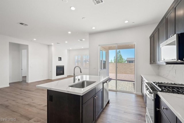 kitchen with light wood-style flooring, a sink, visible vents, appliances with stainless steel finishes, and a glass covered fireplace