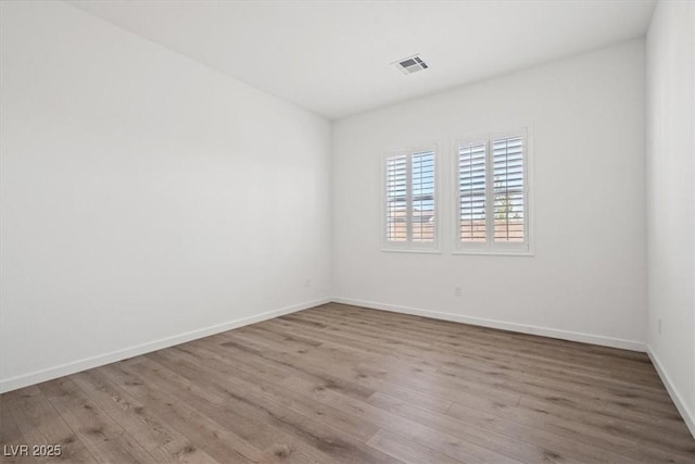 empty room with wood finished floors, visible vents, and baseboards