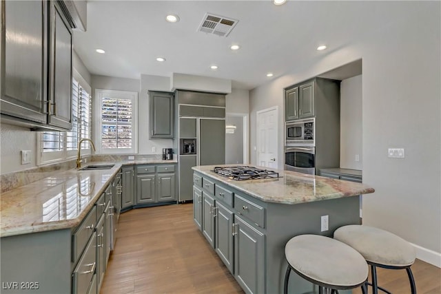 kitchen with built in appliances, a kitchen island, gray cabinets, and visible vents