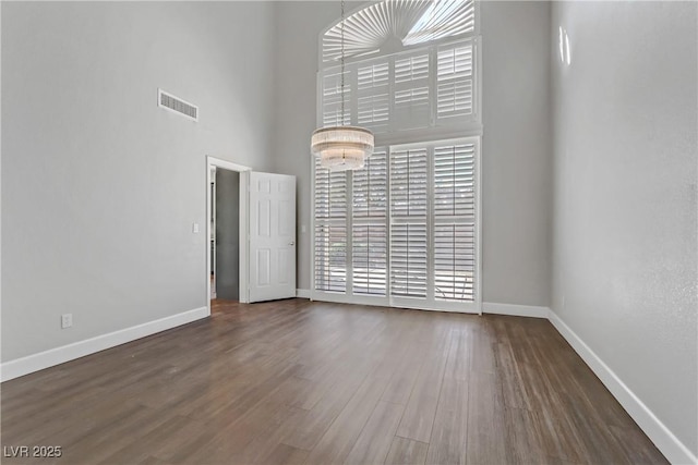 unfurnished room featuring a towering ceiling, baseboards, visible vents, and wood finished floors