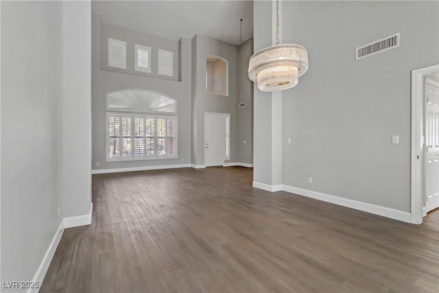 interior space featuring a towering ceiling, baseboards, visible vents, and dark wood finished floors