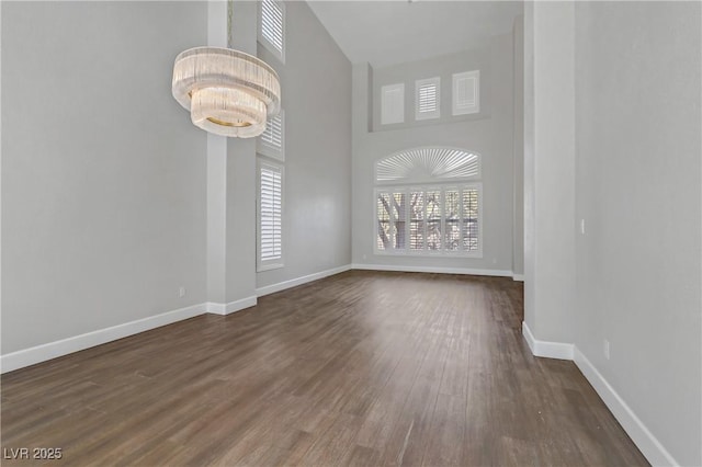 empty room featuring baseboards, a high ceiling, dark wood-style flooring, and an inviting chandelier