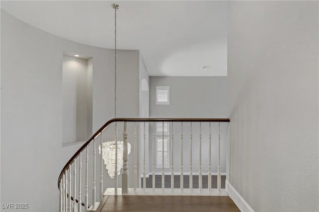 staircase with a notable chandelier, a high ceiling, baseboards, and wood finished floors