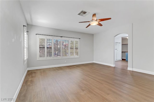 spare room featuring arched walkways, wood finished floors, visible vents, and baseboards