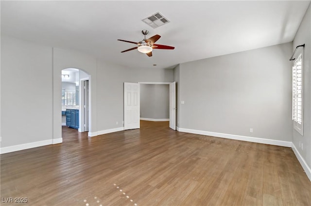 spare room with arched walkways, visible vents, wood finished floors, plenty of natural light, and baseboards