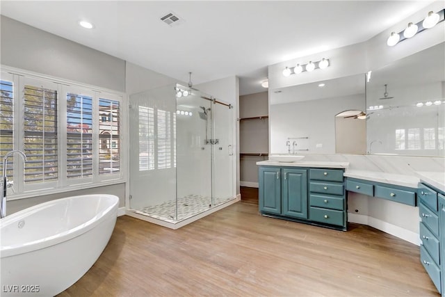 full bathroom featuring a freestanding tub, wood finished floors, vanity, visible vents, and a shower stall