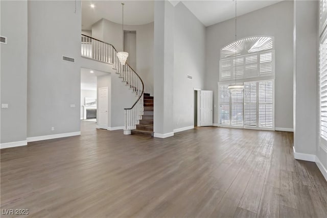 unfurnished living room featuring stairway, wood finished floors, visible vents, and baseboards