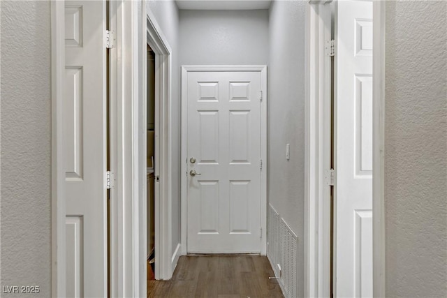 hall with visible vents, wood finished floors, and a textured wall