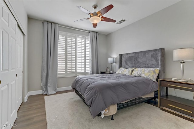 bedroom with ceiling fan, wood finished floors, visible vents, baseboards, and a closet