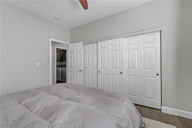 bedroom featuring a closet, washing machine and dryer, ceiling fan, wood finished floors, and baseboards