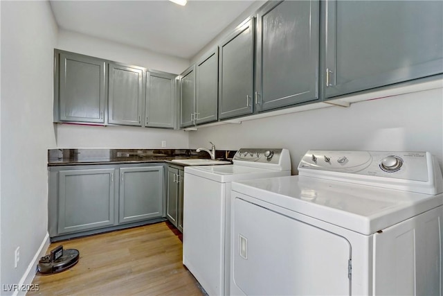 washroom featuring light wood finished floors, cabinet space, a sink, separate washer and dryer, and baseboards