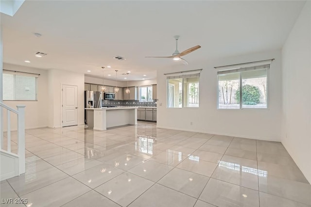 unfurnished living room featuring ceiling fan, a wealth of natural light, light tile patterned floors, and visible vents