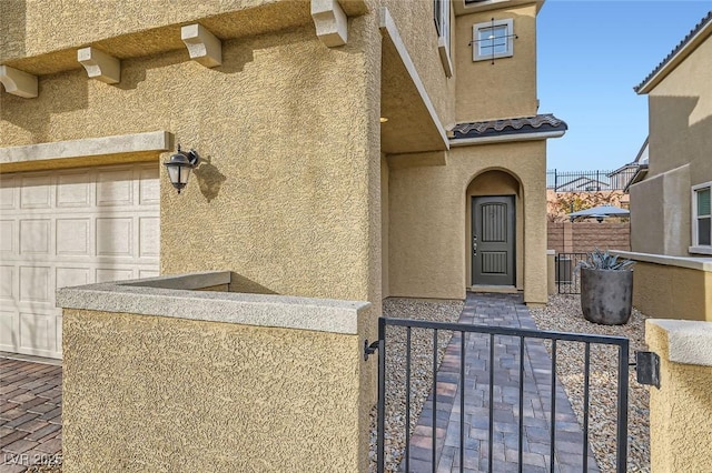 entrance to property featuring an attached garage, a tiled roof, fence, and stucco siding