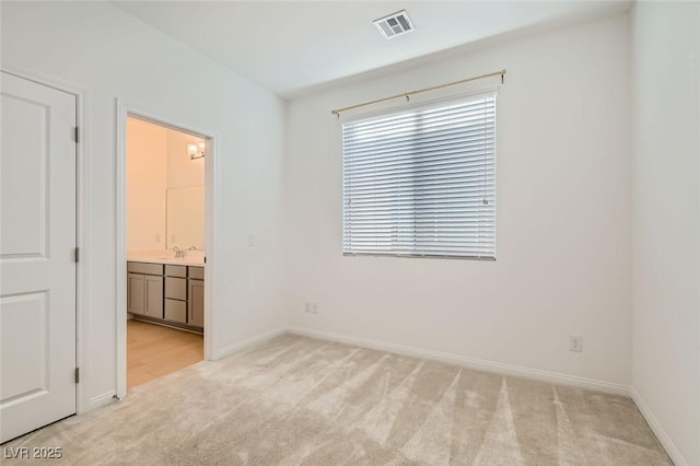 unfurnished bedroom featuring baseboards, visible vents, light colored carpet, ensuite bath, and a sink