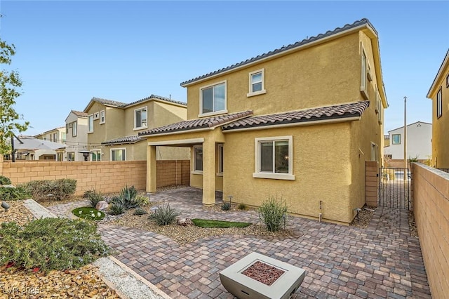 back of house with a tile roof, a gate, fence, a patio area, and stucco siding