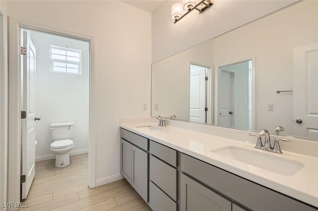 bathroom featuring toilet, double vanity, baseboards, and a sink