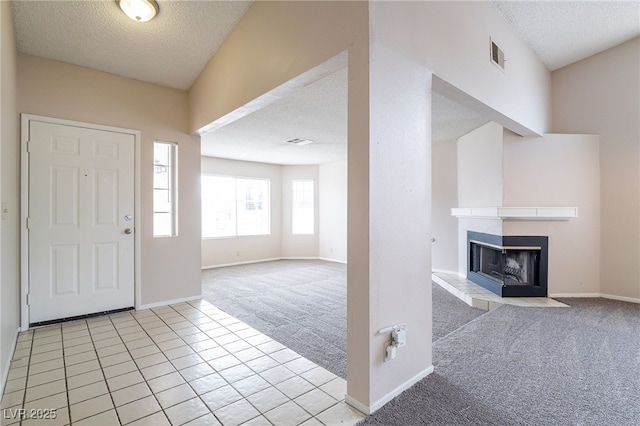 foyer entrance with a fireplace, visible vents, a textured ceiling, and light colored carpet