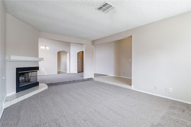 unfurnished living room with visible vents, arched walkways, a textured ceiling, carpet flooring, and a multi sided fireplace