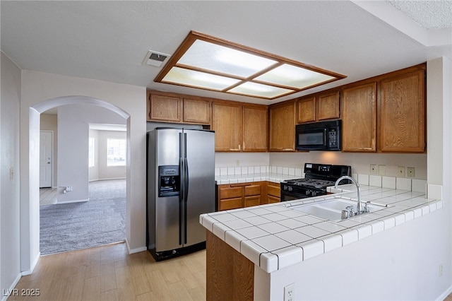 kitchen with visible vents, tile counters, brown cabinets, a peninsula, and black appliances