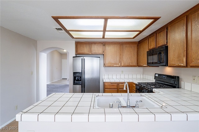 kitchen with tile countertops, visible vents, a sink, a peninsula, and black appliances