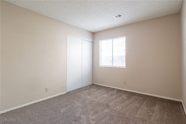 unfurnished bedroom featuring baseboards, visible vents, a textured ceiling, carpet flooring, and a closet