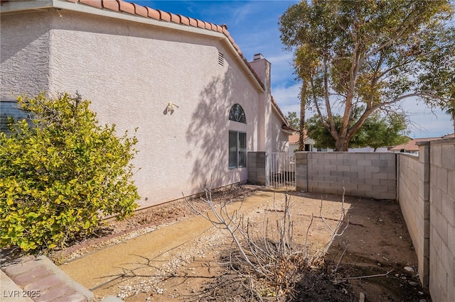 view of home's exterior with a gate, fence, a chimney, and stucco siding