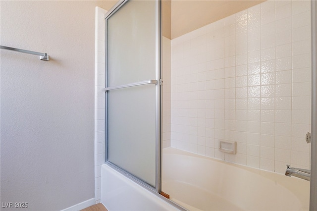 bathroom featuring baseboards, combined bath / shower with glass door, and a textured wall