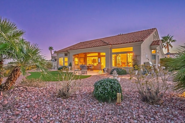 back of house at dusk with a tiled roof, a patio area, and stucco siding