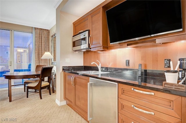 kitchen with a sink, ornamental molding, light wood-type flooring, brown cabinetry, and stainless steel microwave