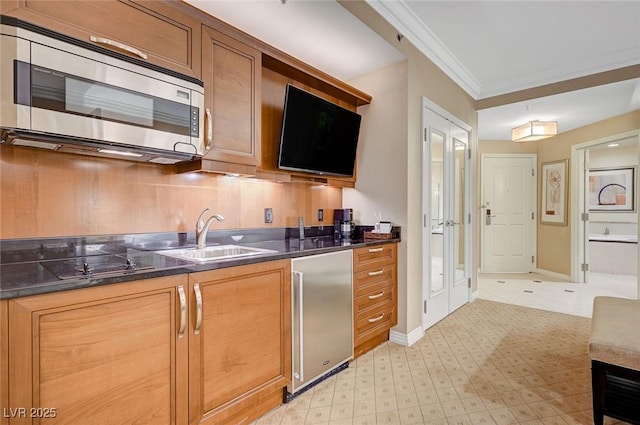 kitchen with crown molding, dark countertops, appliances with stainless steel finishes, brown cabinetry, and a sink