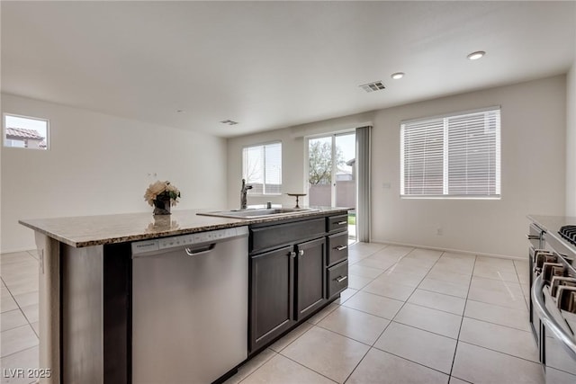 kitchen with light tile patterned floors, a sink, visible vents, appliances with stainless steel finishes, and a center island with sink