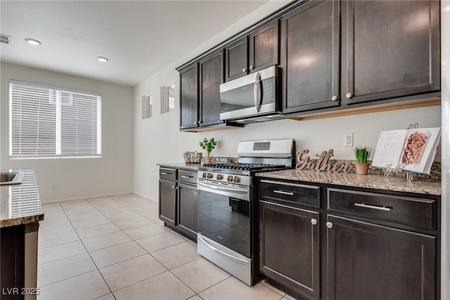 kitchen featuring light tile patterned flooring, dark brown cabinetry, stainless steel appliances, visible vents, and light stone countertops