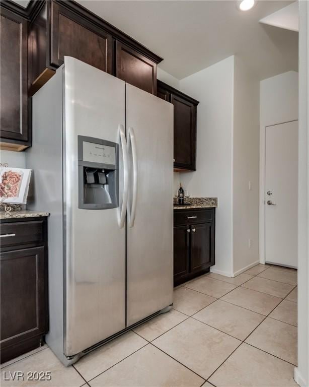 kitchen with light tile patterned flooring, stainless steel fridge, dark brown cabinetry, and light stone countertops