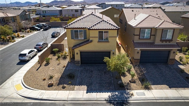 view of front of property featuring a garage, a residential view, decorative driveway, a mountain view, and stucco siding