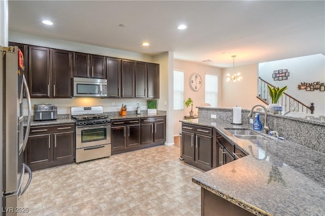 kitchen with dark brown cabinetry, dark stone countertops, appliances with stainless steel finishes, and a sink