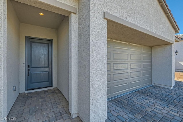 view of exterior entry with stucco siding and a garage