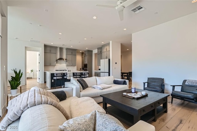 living room featuring a ceiling fan, visible vents, baseboards, light wood-style flooring, and recessed lighting