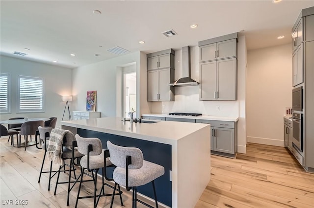 kitchen with a sink, gray cabinetry, black gas cooktop, and wall chimney range hood