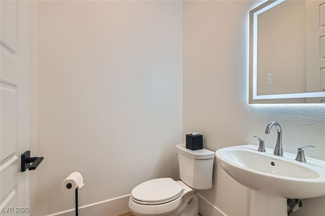 half bathroom with toilet, baseboards, and a sink