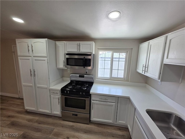 kitchen with dark wood-style floors, appliances with stainless steel finishes, light countertops, white cabinetry, and a sink