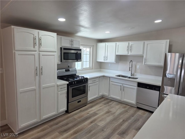 kitchen with white cabinets, appliances with stainless steel finishes, light countertops, light wood-style floors, and a sink