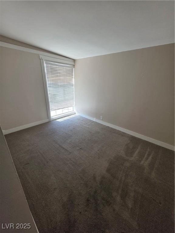 spare room with dark carpet and baseboards