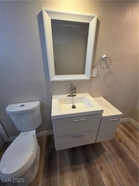 half bath featuring toilet, baseboards, wood finished floors, and vanity